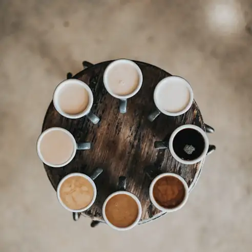 Eight cupping bowls arranged in a circle on a wooden table, each with a different roast.