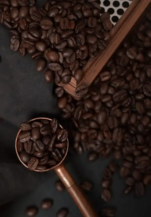 A copper scoop of roasted beans resting on a pile of them.