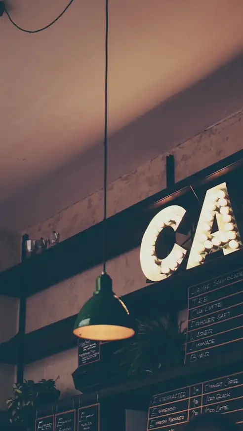 A cafe interior at night, lit by pendant lamps and a sign made of bulbs.